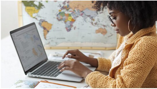 Young Black woman typing on laptop, large world map in the background